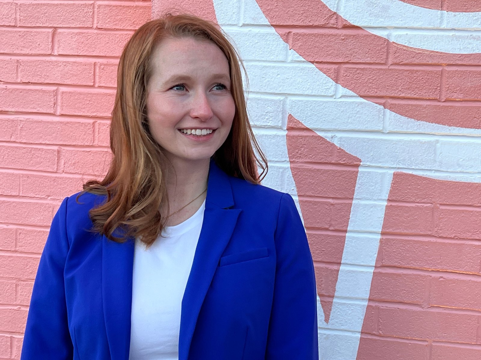 Caitlyn Gegen smiling warmly in front of a pink and white star mural